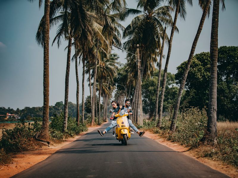 Smiling couple travelling on a scooter along a palm-lined road